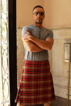 Man in a red and brown tartan kilt and grey T-shirt, front view in a doorway
