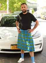 Man in bright blue, green and yellow tartan kilt standing in front of a car