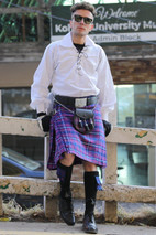 Man in purple tartan kilt with sporran and ghillie shirt leaning on a railing