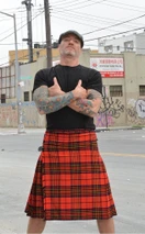 Man in red and black tartan traditional kilt with arms crossed on a city street