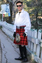 Man wearing red Bruce tartan kilt and sporran by a white fence, three-quarter view