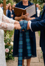 Couple's hands bound with a blue and green tartan handfasting ribbon at an outdoor wedding