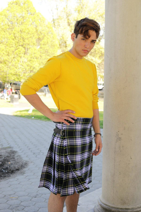 Young man in black, white and lilac tartan kilt with yellow sweater by a column