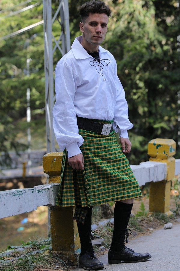Young man in green and yellow tartan kilt with white ghillie shirt outdoors