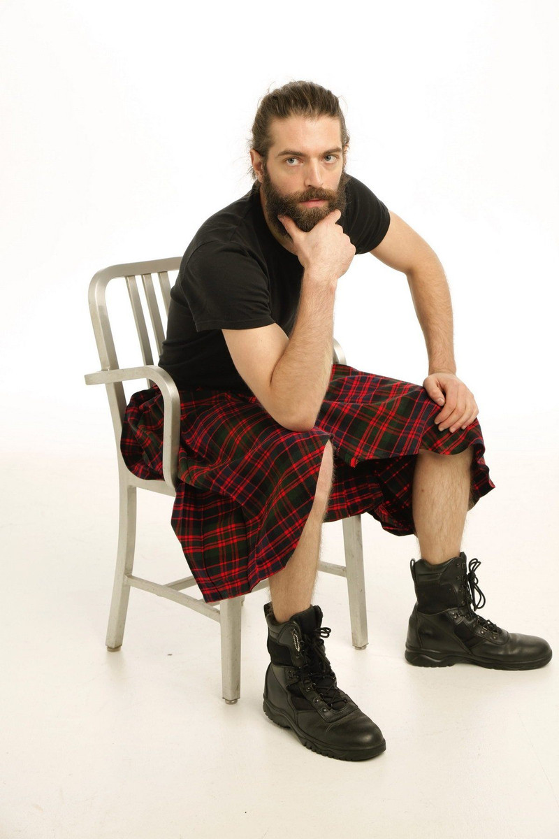 Man seated on chair in red and black tartan crossover kilt