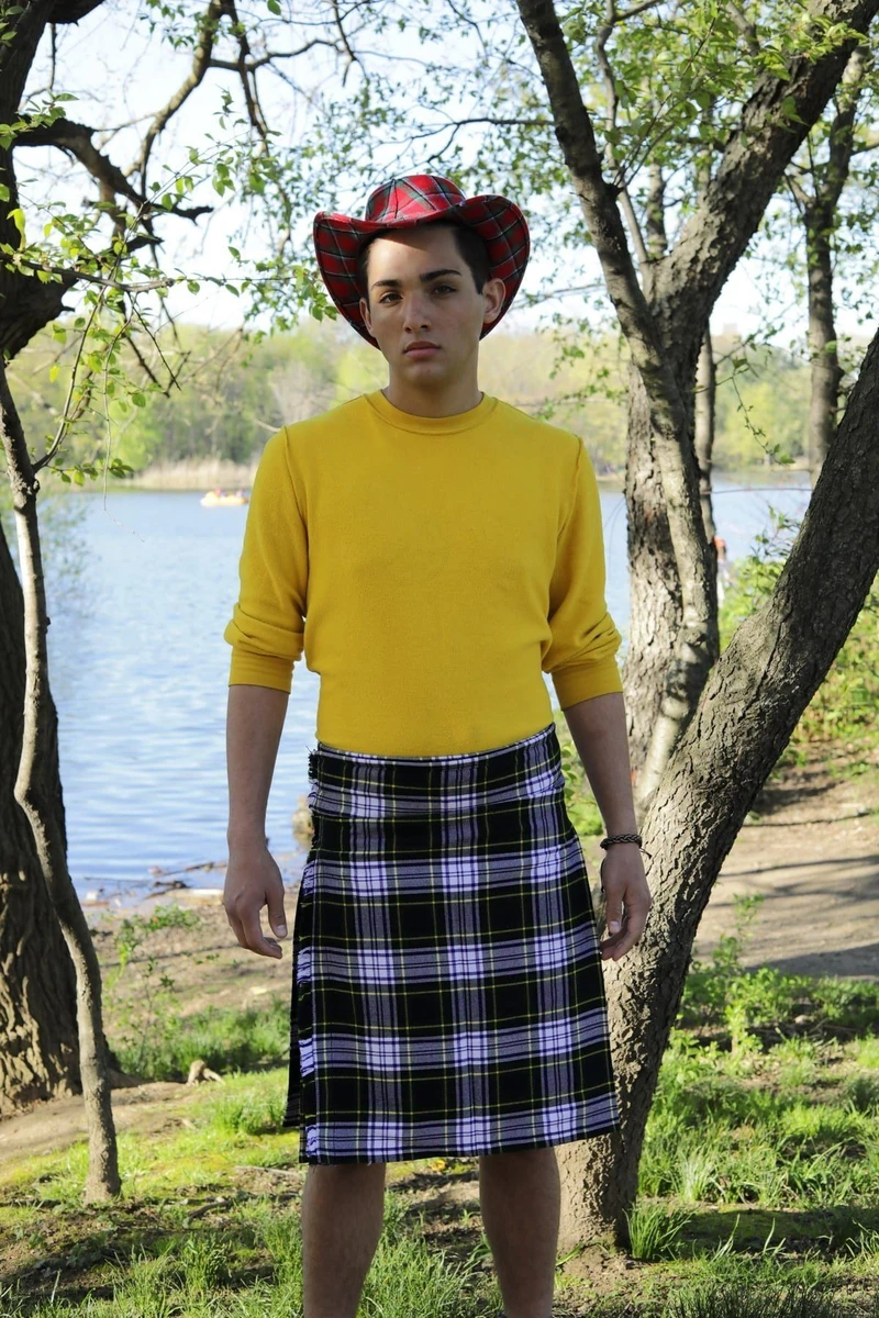 Front view of black, white and lilac tartan kilt worn with yellow top outdoors