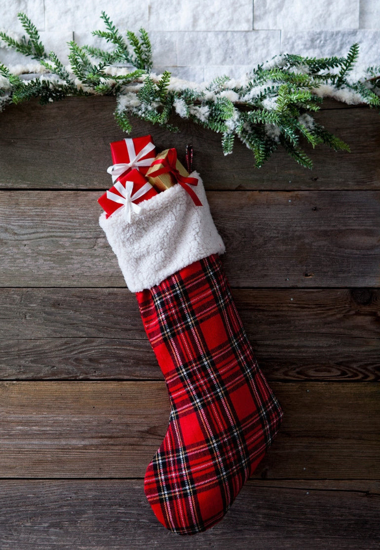Christmas stocking in red tartan with white cuff filled with gifts, hanging on a wooden wall