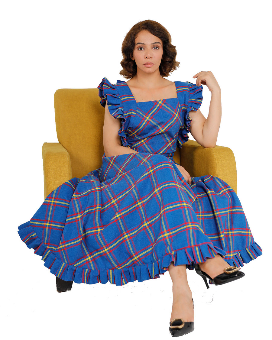 Woman seated in yellow armchair wearing blue tartan maxi dress with ruffle hem