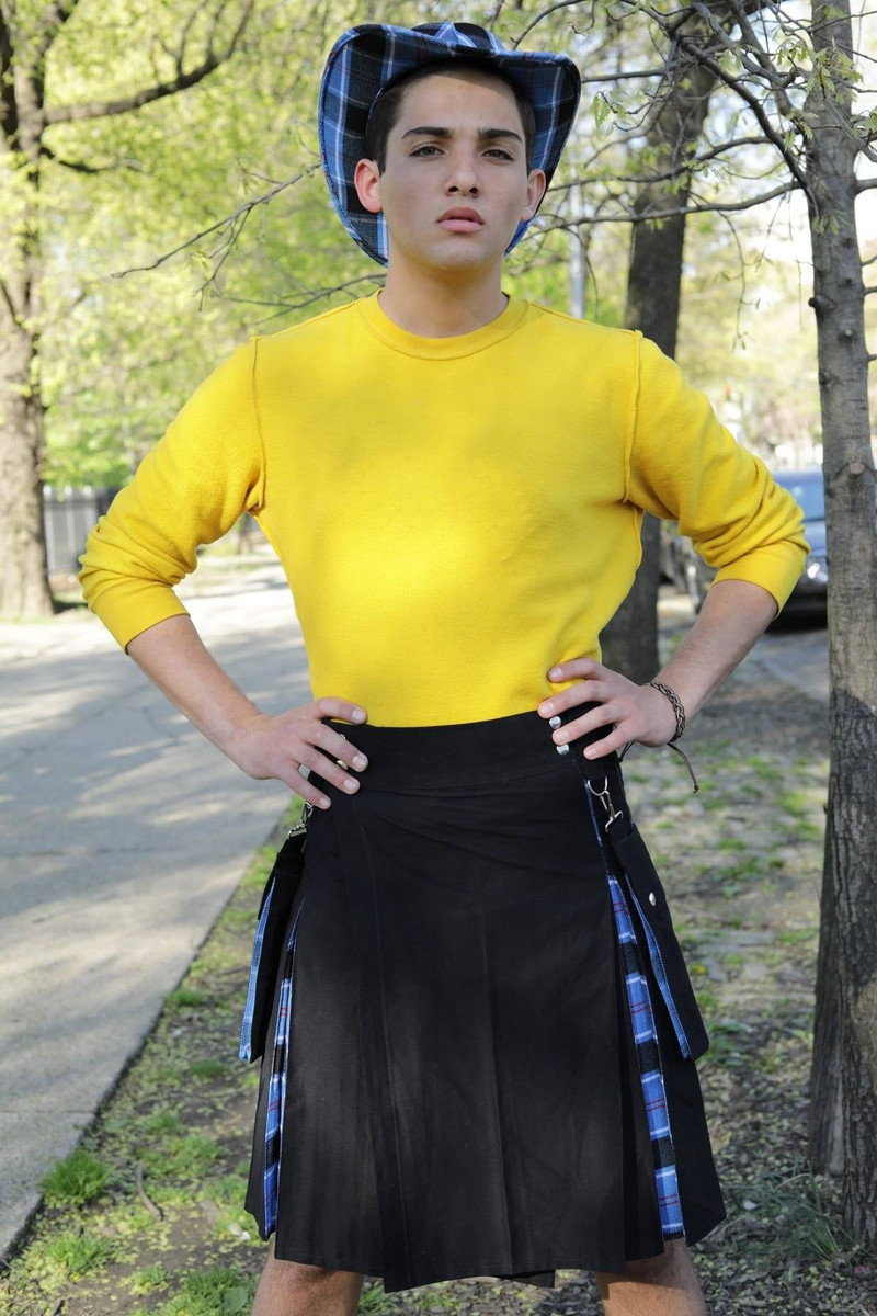 Man in black hybrid kilt with blue tartan pleats and matching tartan hat, outdoors