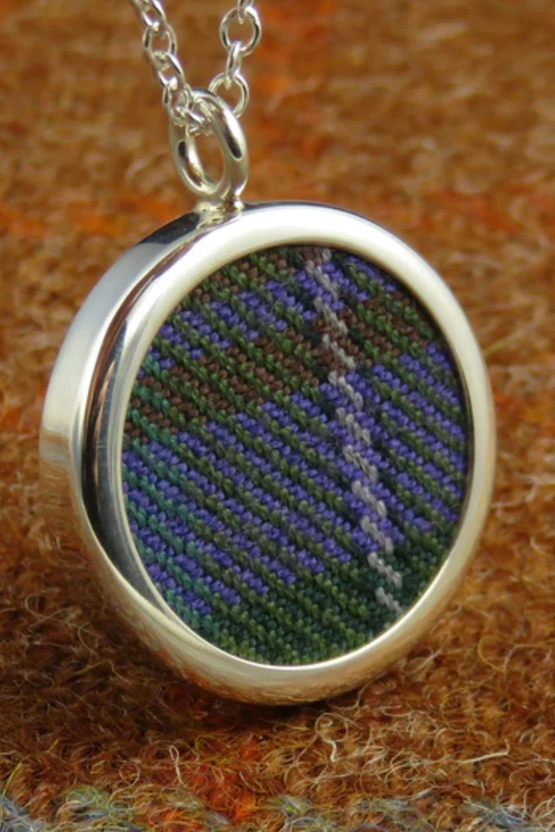 Round silver pendant with purple and green tartan insert on a chain