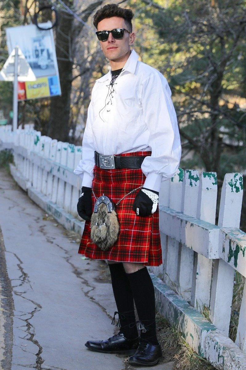 Man wearing red Bruce tartan kilt and sporran by a white fence, three-quarter view