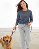 A woman walks a golden retriever on the beach, wearing a dark grey long-sleeve tee and grey sweatpants.
