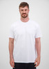 A man wearing a plain white short sleeve tee, standing against a neutral background. The tee features a logo.