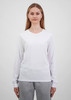 A woman wears a white long sleeve tee, paired with grey trousers. The tee features a simple design and has a logo.