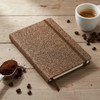 A brown notebook with a cork-like cover, accompanied by coffee beans, ground coffee, and a cup of coffee.