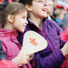 A foldable event fan in cream, held by a girl, with a logo displayed, surrounded by cheering spectators.