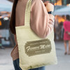 A yellow cotton tote bag with a logo, worn over the shoulder by a person in a casual outfit.