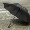 A black umbrella with a curved handle and a logo on its canopy, resting on a wet surface.