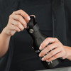 A drink bottle in matte black with a carry lid, held in a person's hand. It features a logo.