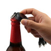 A drink bottle opener with a black circular design and attached charging cables is being used to open a red bottle cap.