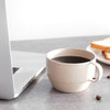 A reusable wheat straw coffee cup in a beige colour sits beside a laptop, with coffee and toast nearby.