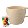 A drink bottle in a beige wheat straw cup alongside a bag of colourful jelly beans. The cup features a handle and a textured finish.