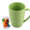 A reusable coffee cup in pastel green with a handle, accompanied by a packet of colourful jelly beans.