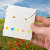 A hand holds a white sticky note pad with coloured circles on the front, set against a vibrant flower field background.