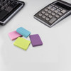 A collection of four rubber erasers in pink, blue, green, and purple, resting on a grey surface near a calculator and keyboard.