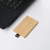 A bamboo USB flash drive in a rectangular shape, resting beside a laptop on a white surface. It features a branding logo.