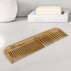 A bamboo comb in natural tones with a branded logo, placed on a marble surface next to a soap bar.
