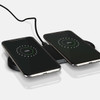 A sleek black dual wireless charger with two smartphones displaying charging indicators.