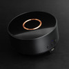 A wireless charging speaker in black with a glossy finish and a copper accent on top, featuring control buttons and a logo.
