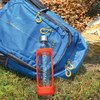 A drink bottle with a clear body and red silicone sleeve is positioned in front of a blue backpack.
