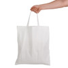 A white cotton tote bag with short handles is held by a hand. The bag features a simple design and a blank surface.