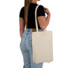 A woman holds a natural-coloured calico tote bag over her shoulder, featuring long handles and a simple design.