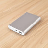 A silver power bank with a USB port on a wooden surface, featuring a sleek, minimal design and a logo.