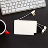 A white 5,000mAh power bank with built-in charging cables, placed on a dark surface near a keyboard and a mug.