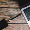 A black charging cable connects a device to a silver laptop on a wooden surface.