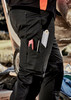 Men's work pants in black, featuring multiple pockets for tools and a visible logo, set outdoors.