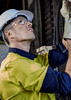 A man in a yellow and navy long sleeve shirt with a helmet and safety glasses, examining equipment.