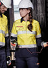 A yellow and navy safety shirt with hooped reflective tape, featuring a logo, worn by a woman in a construction setting.