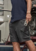 Men's rugged stretch shorts in dark grey, featuring cargo pockets and a sleek design, held by a person with a tool.