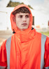 An orange heavy-duty waterproof jacket with reflective strips, featuring a hood and a zippered collar, worn by a model.