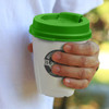 A drink bottle with a white body and a green lid, held in a hand outdoors. It features a logo on the side.