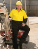 A man wearing a bright yellow and black long-sleeve safety shirt stands beside construction equipment. The shirt features a logo.