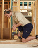A man in khaki and navy work shorts operating a drill, wearing ear protection, in a construction setting.