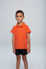 An orange polo shirt for kids displayed on a child, paired with black shorts, featuring a logo on the shirt.