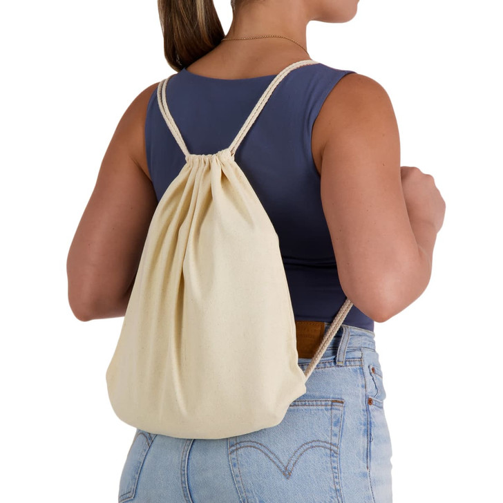 A cream-coloured drawstring backpack is worn on the back of a person, featuring simple cord straps and a gathered top.