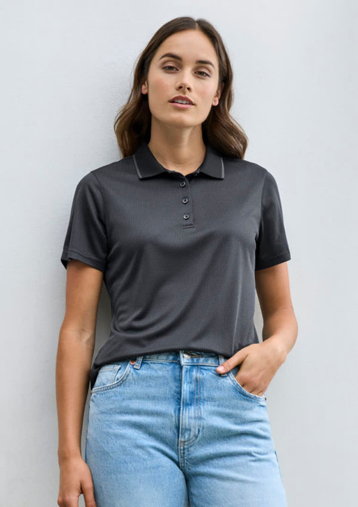 A women's short sleeve polo shirt in black, featuring a collar and a button placket, paired with light blue jeans.